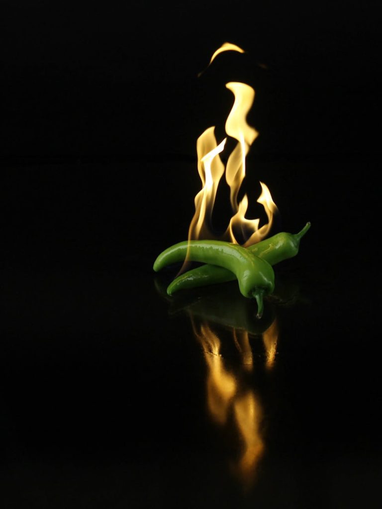 Dynamic image of green chili peppers engulfed in flames over a dark reflective surface.