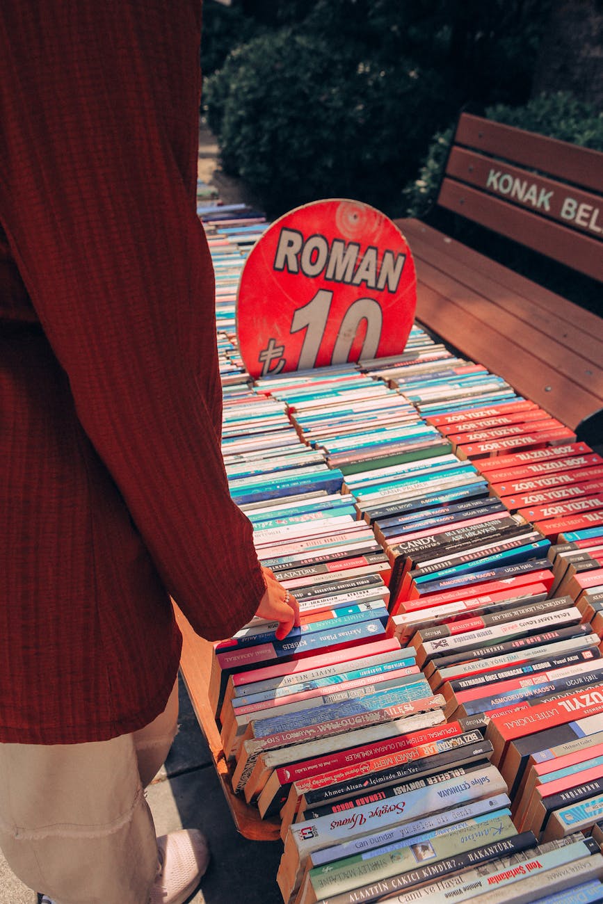 Person browsing books at an outdoor book stall with vibrant roman signage and pricing.