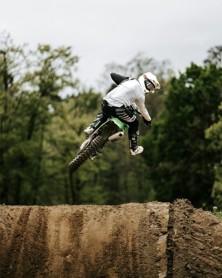 Daring motocross biker executing a high jump in a dense forest terrain.