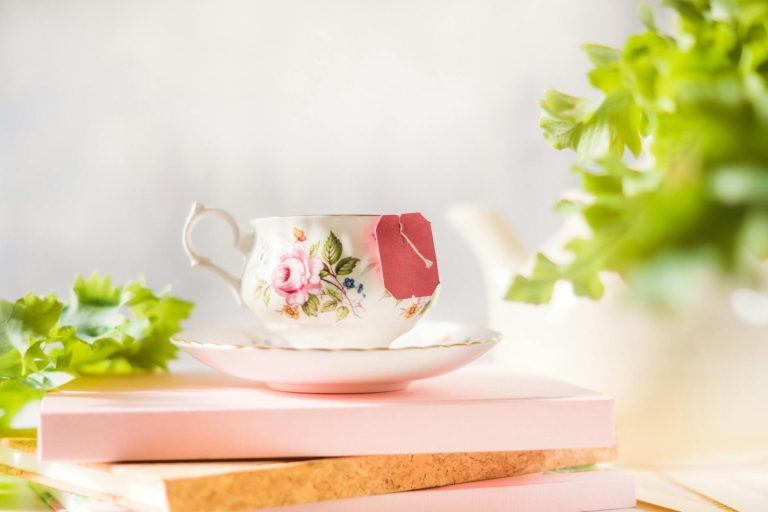 Charming floral teacup with a tea bag resting on books, surrounded by greenery.