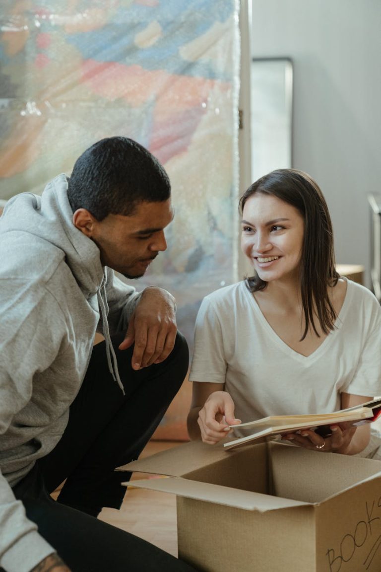 A cheerful couple unpacks books while moving into their new apartment, showing the excitement of a fresh start.