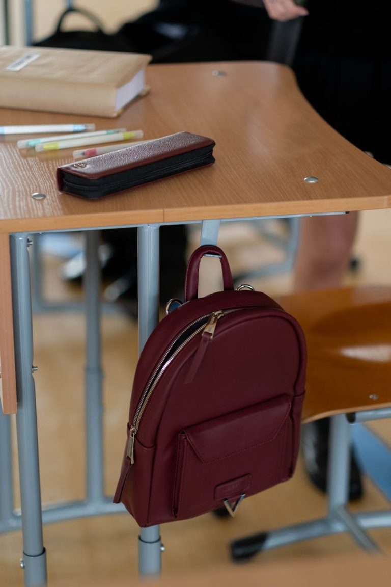 A red school backpack hanging on a desk in a classroom setting.