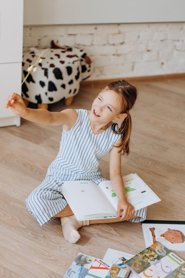 A smiling girl enjoying reading books on the floor indoors, exuding happiness and curiosity.