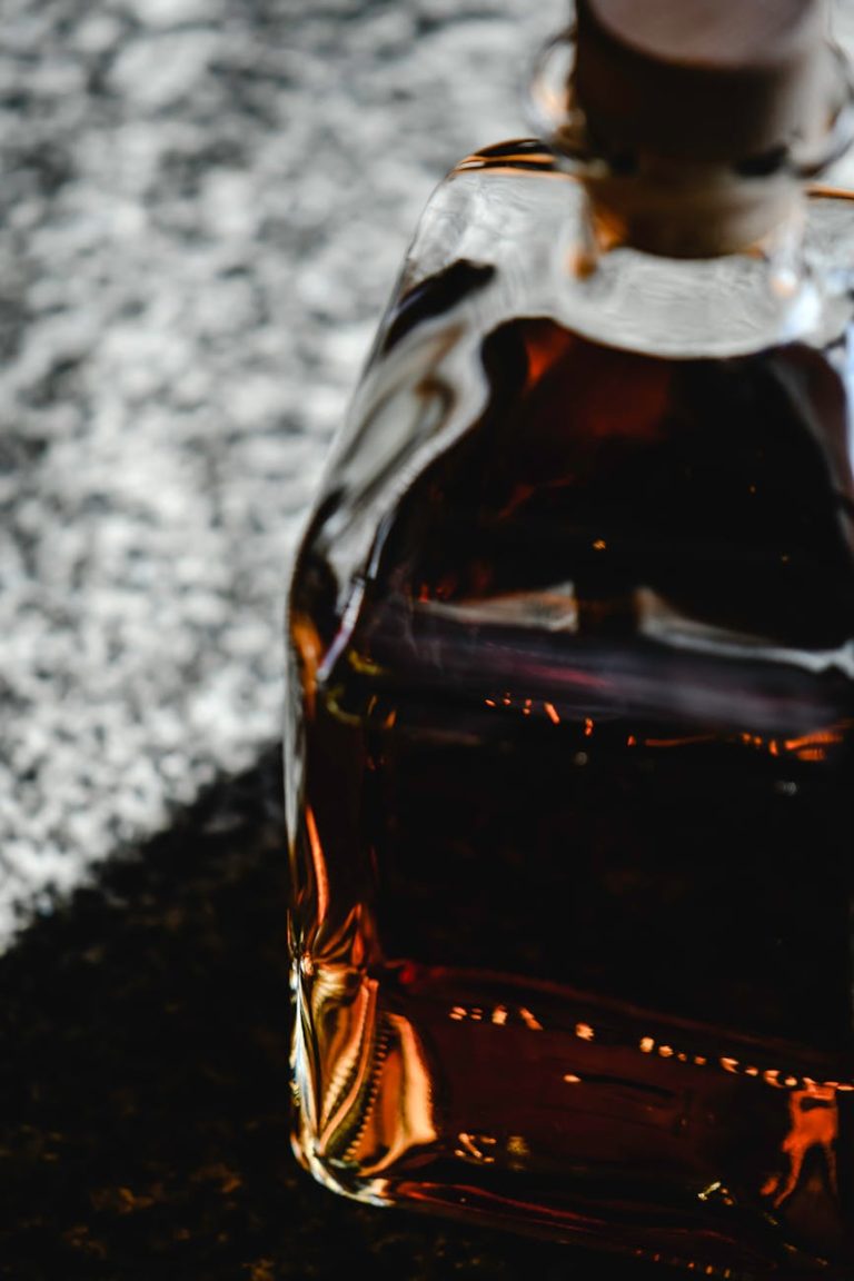 Close-up image of a whiskey bottle on a reflective surface, highlighting its rich amber color.