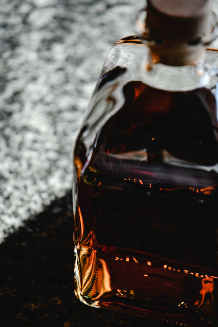 Close-up image of a whiskey bottle on a reflective surface, highlighting its rich amber color.