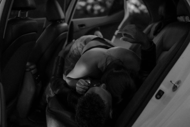 A romantic black and white scene depicting a couple in an intimate embrace inside a car.