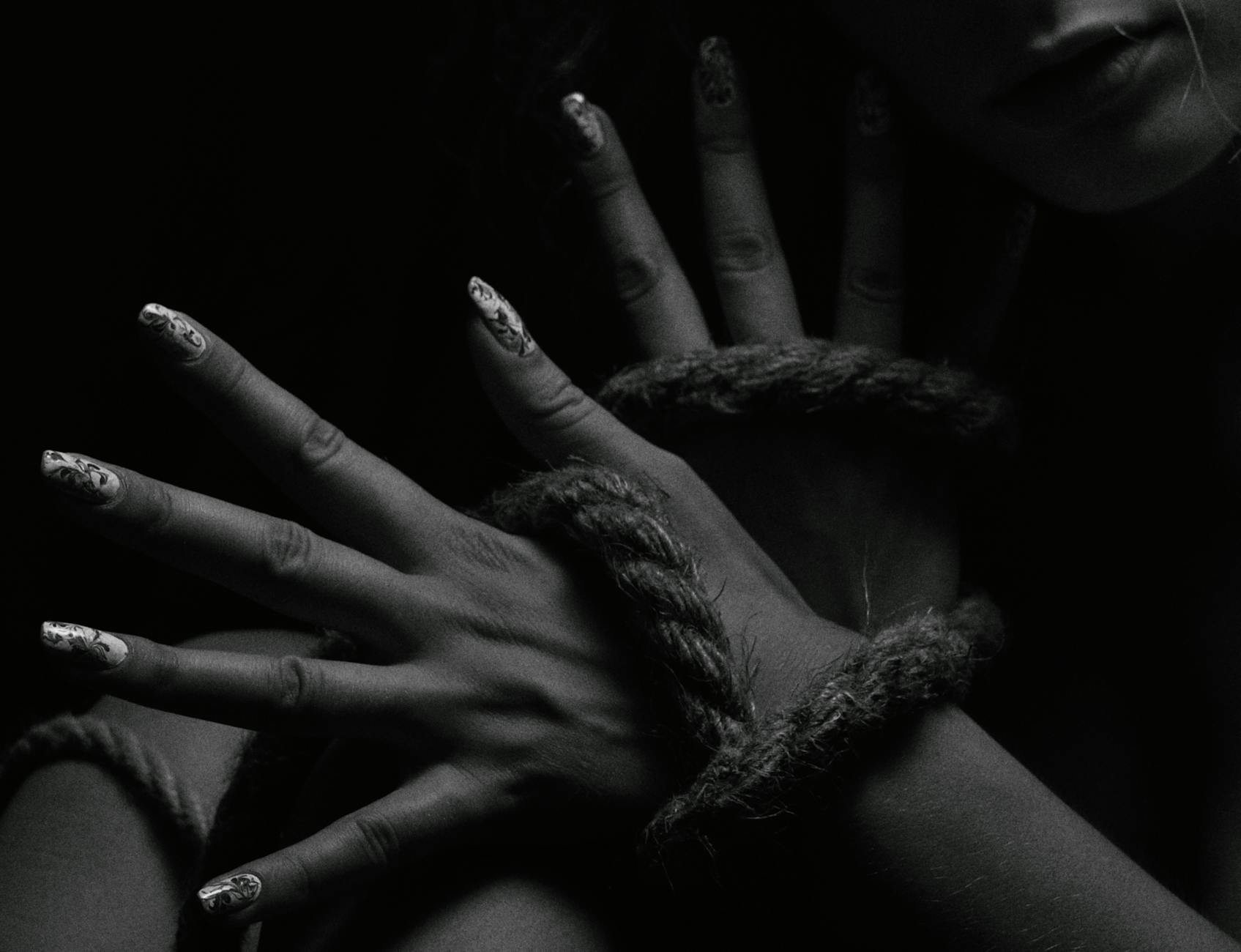 Black and white photo of hands intertwined with rope. Dramatic and artistic close-up.