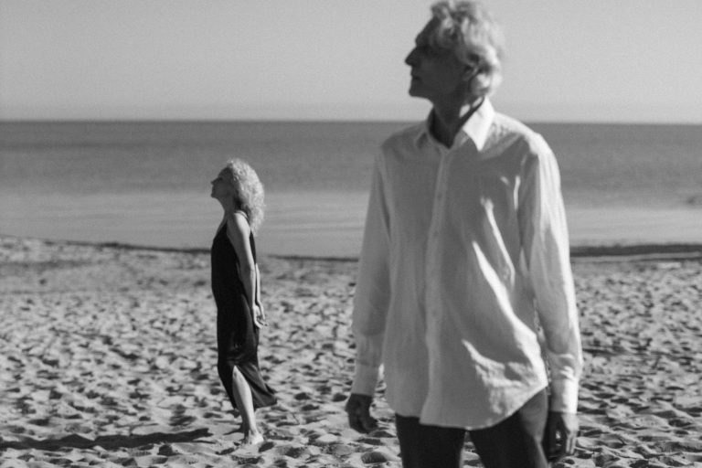 An elderly couple walking on a serene beach, captured in monochrome, embracing tranquility.