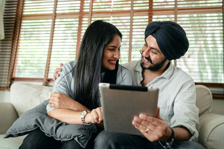 A joyful couple using a tablet indoors, embracing and smiling together.