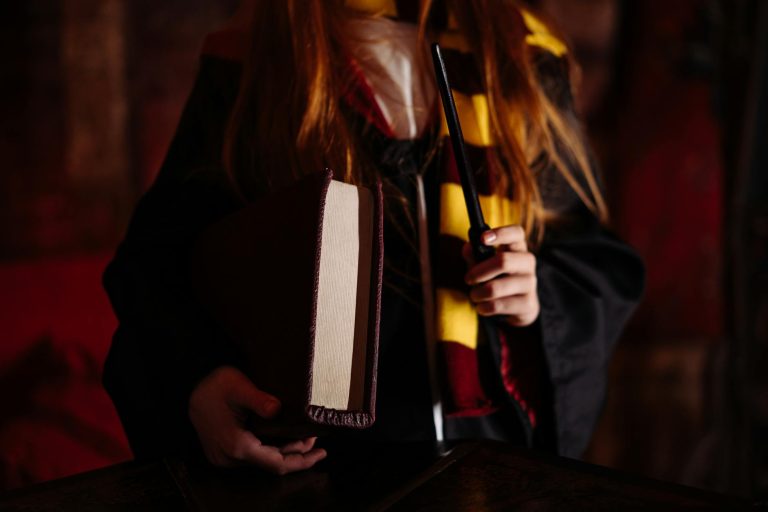 A girl in a wizard costume holding a wand and book, evoking magical themes.